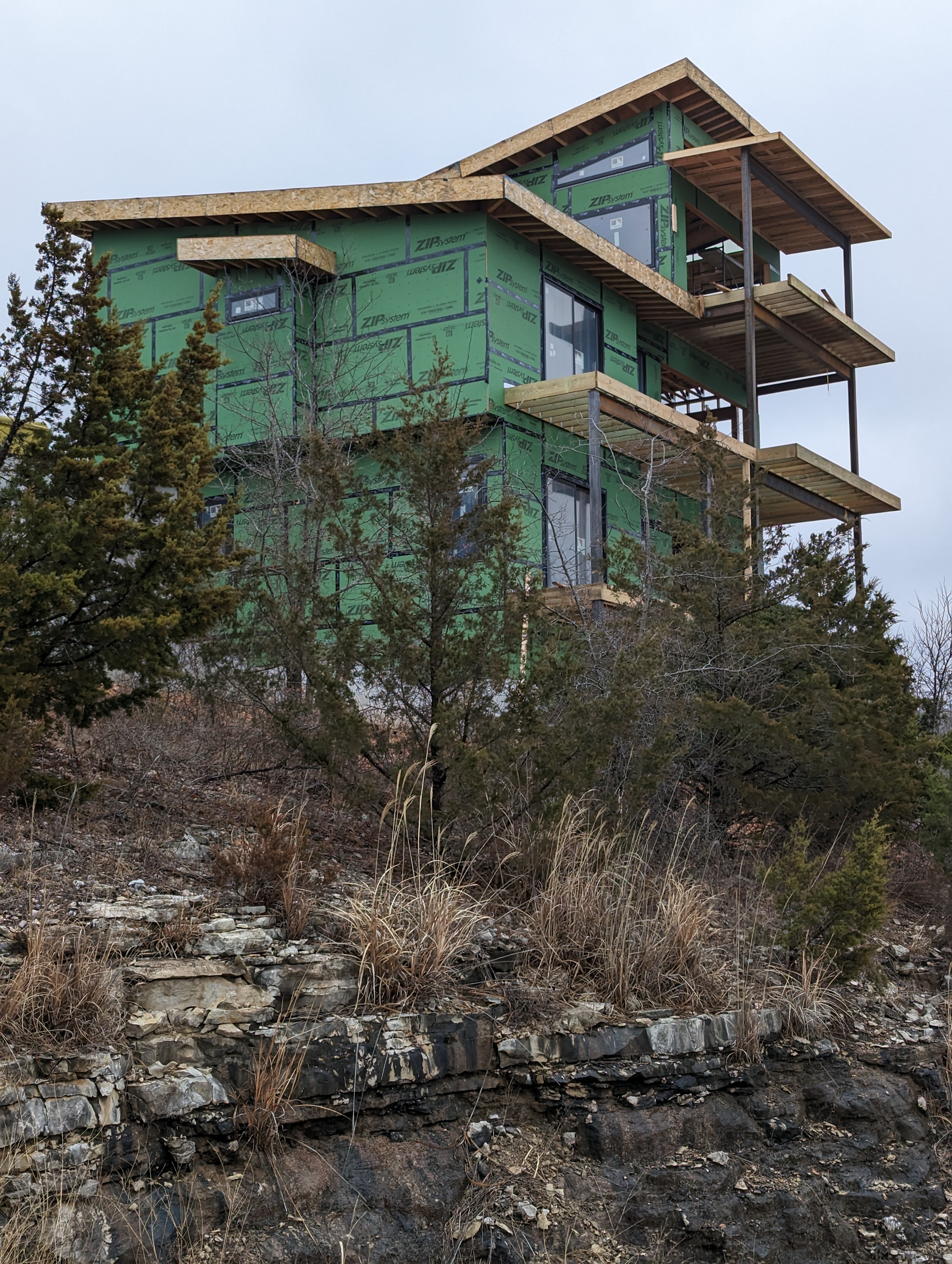 Rear view of modern home under construction. Home is 3 stories, including the walk-out basement, and has single-pitch rooflines and is comprised of several boxy volumes.